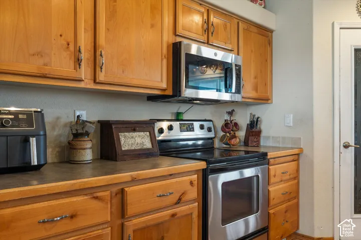 Wood cabinetry with decorative hardware, stainless steel overhead microwave, stainless steel electric range, and solid surface countertops