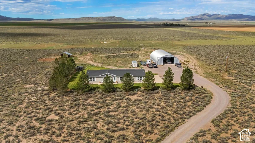 Gabled-roof residence with a covered porch, detached storage building, and an expansive metal arch-span structure, all surrounded by open terrain