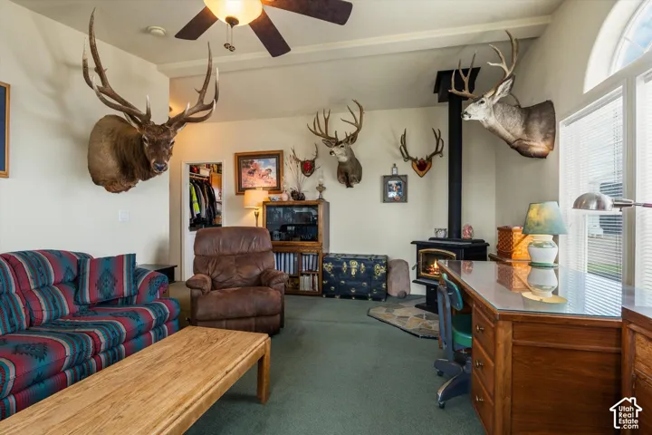 Vaulted ceiling with ceiling fan, wood-burning stove with black stovepipe, large arched window, built-in shelving, and a wood-finish desk