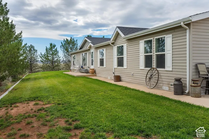 Vinyl siding exterior with white window shutters, concrete patio, and a sloped lawn