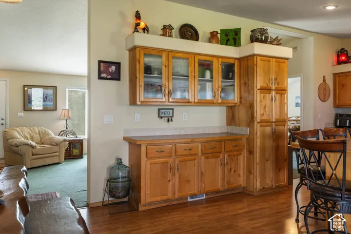 Wood-finish flooring, built-in wooden cabinetry with glass-front uppers, and a built-in pantry