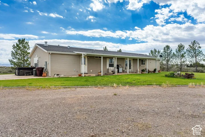 Expansive gravel driveway, covered patio, and grassy yard with mature trees