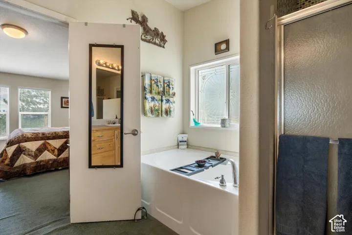 Built-in soaking tub with deck-mounted faucet, privacy window with decorative glass, and a glass-enclosed shower with a mosaic tile border