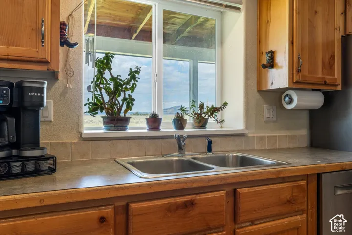 Dual basin stainless steel sink with a single-lever faucet, solid surface countertops, light-toned wood cabinetry, and a tile backsplash
