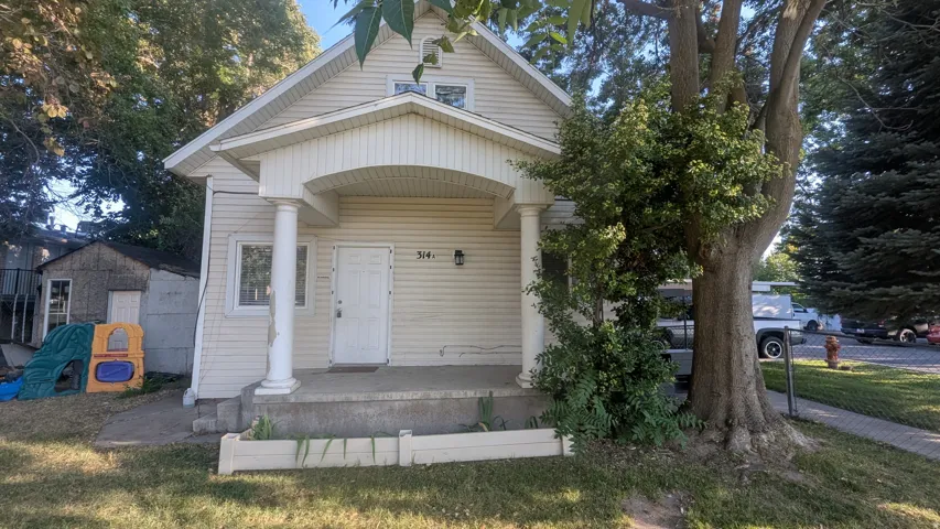 Covered front porch with column supports, white siding, and prominent mature trees