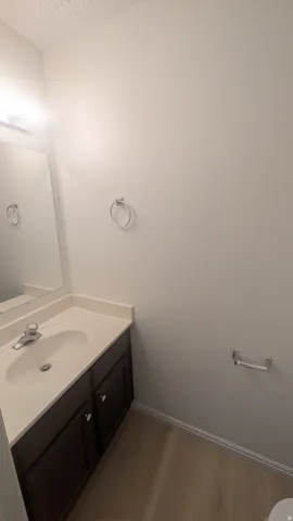 Vanity with an integrated sink, polished chrome faucet, wood-finish flooring, and wall-mounted mirror