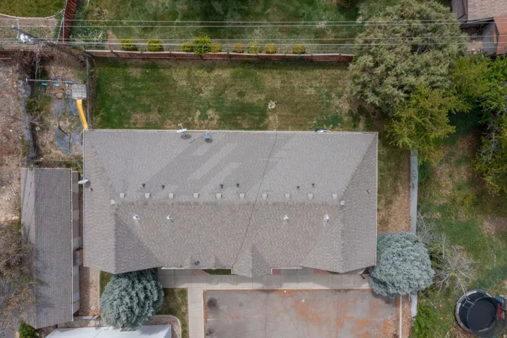 Shingle roof structure with multiple vents, established trees, and a grassy lawn area