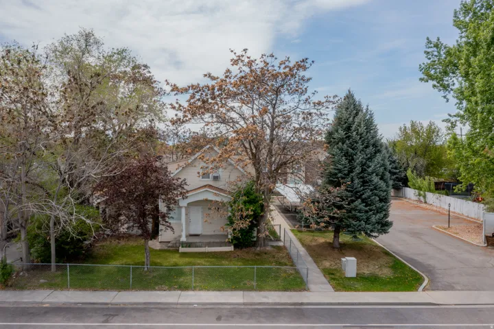 SSisding exterior with a covered front porch, mature trees, a paved driveway, and a chain-link fence bordering a sidewalk