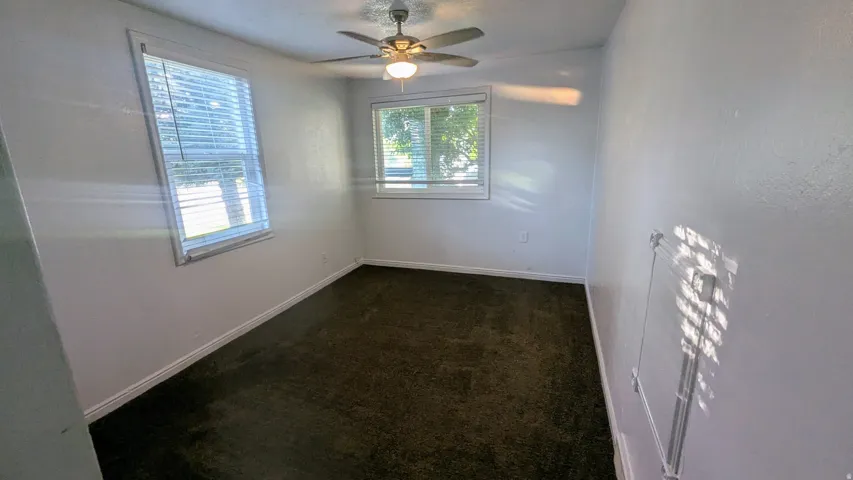 White painted walls, dark carpeting, and a ceiling fan with integrated lighting
