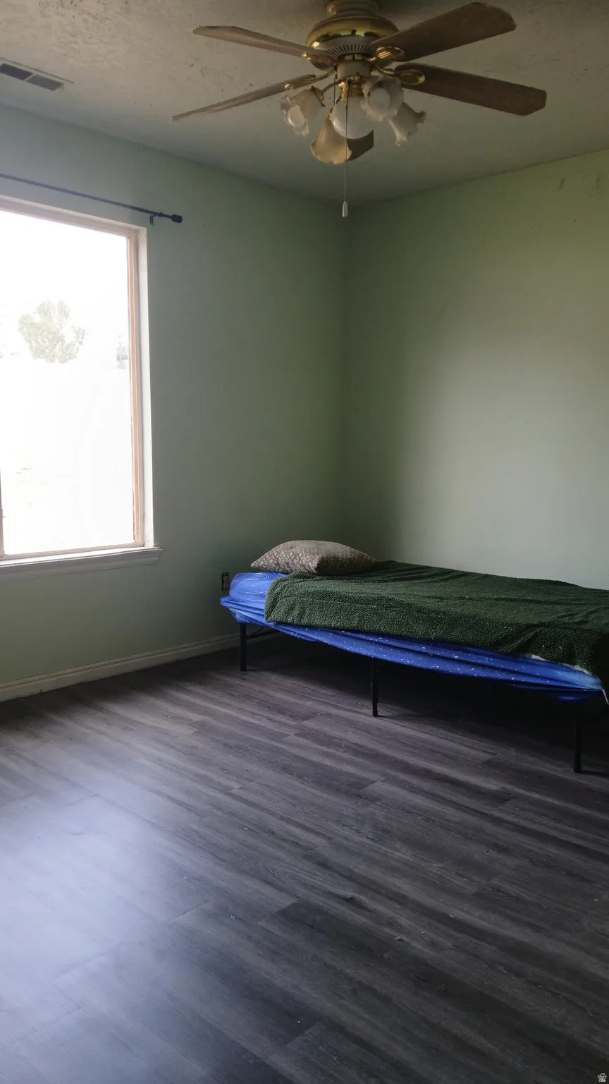 Wood-finish flooring, ceiling fan with integrated lighting, and a single window with a dark-finish curtain rod