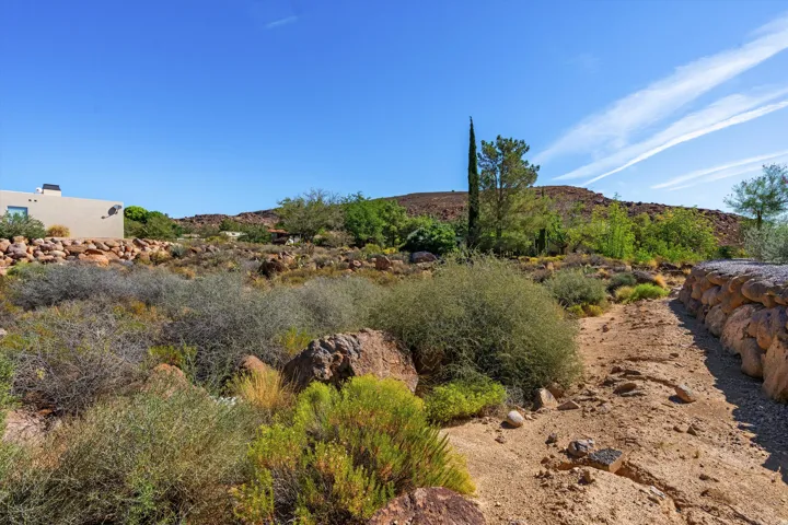 Natural desert landscaping with a stone retaining wall, expansive rocky terrain, and a distant stucco exterior structure