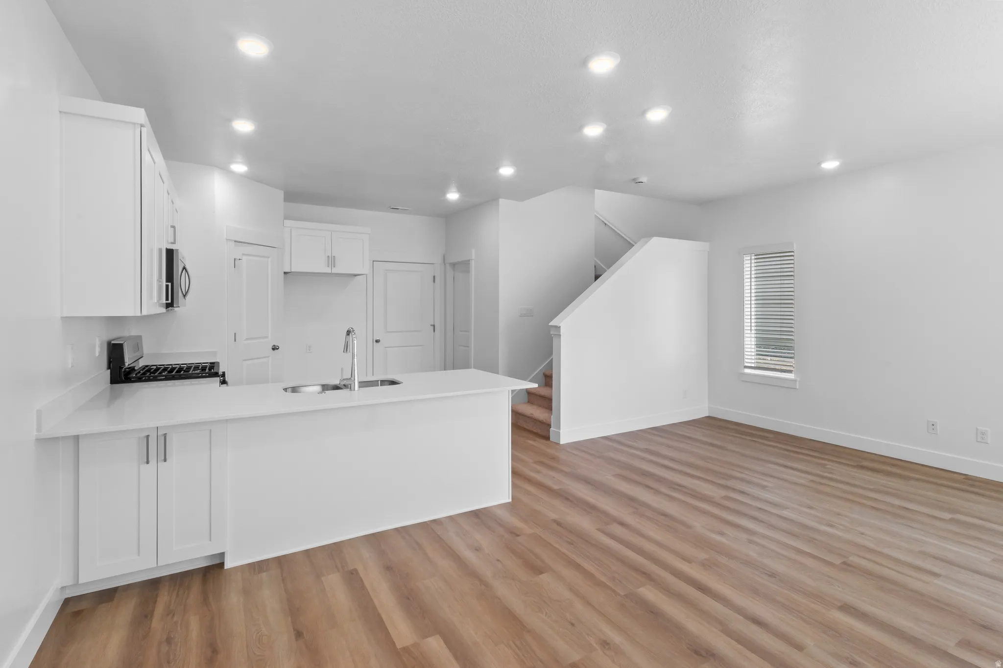 Open-concept living space with wood-finish flooring, white cabinetry, a kitchen island with an undermount sink, and recessed lighting
