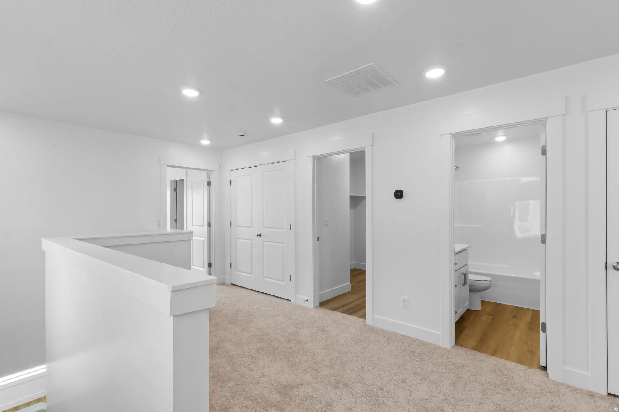 Loft area featuring neutral carpeting, white interior doors, bright recessed lighting, a built-in closet, and a full bathroom with a white vanity and tub/shower combination