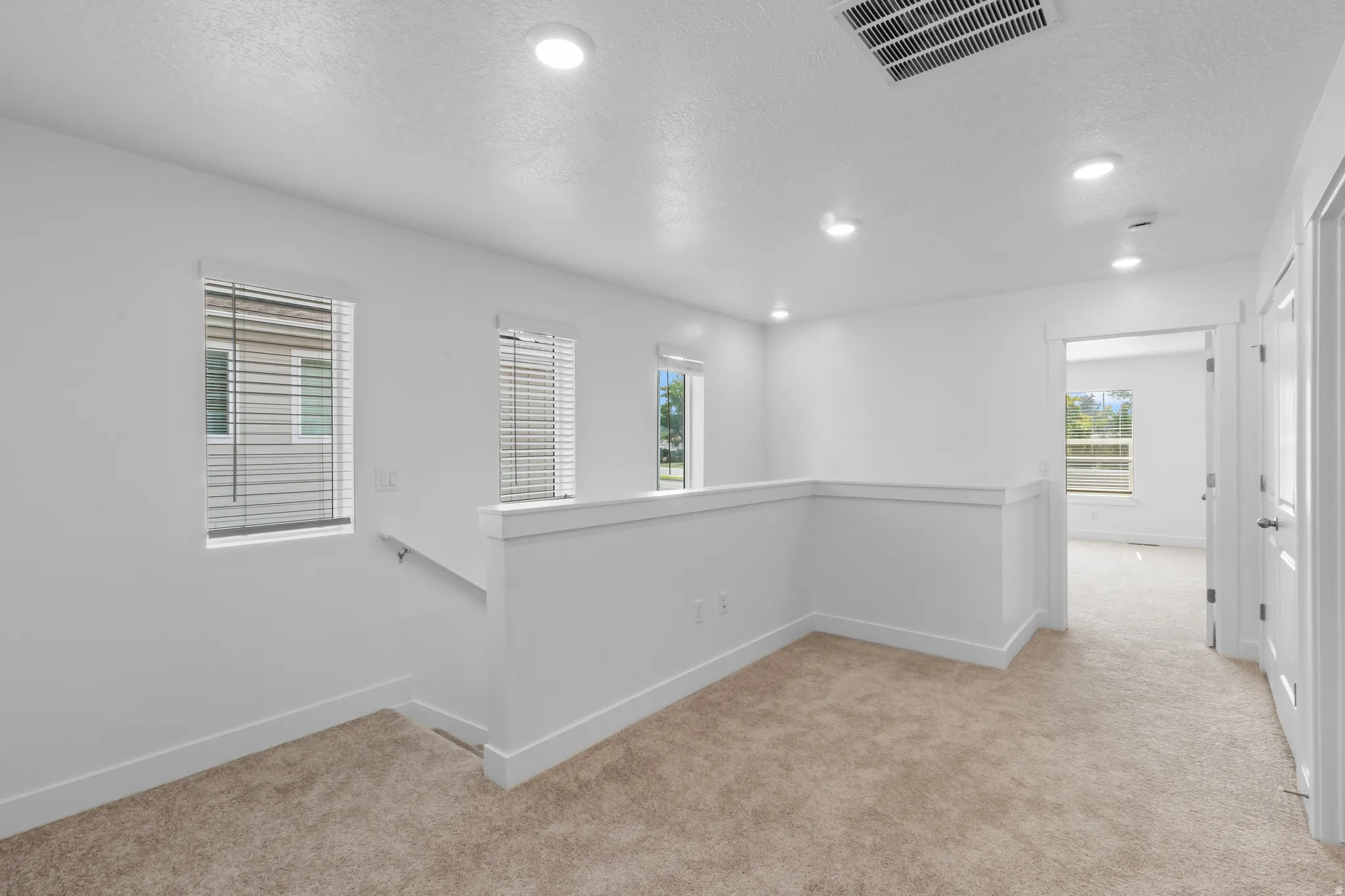 Open loft area featuring neutral carpeting, recessed lighting, white walls, and multiple windows with blinds