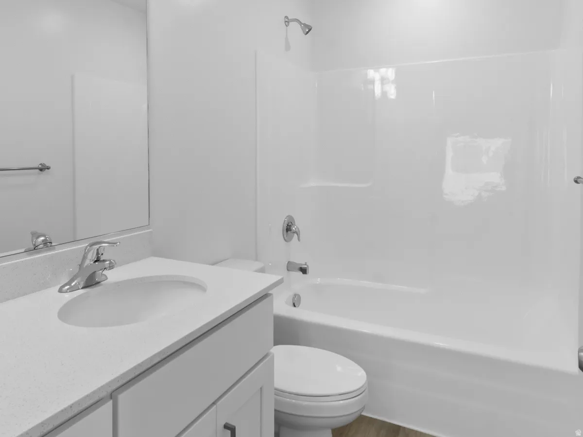 Bathroom featuring a white vanity with integrated sink, chrome faucet, white bathtub with shower, and wood-finish flooring