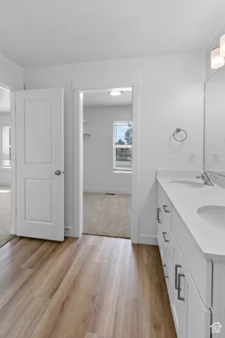 Dual vanity with white cabinetry and integrated sinks, wood-finish flooring, and wall-mounted light fixtures