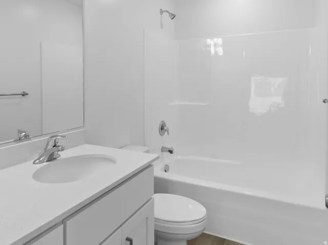 Bathroom featuring a white vanity with integrated sink, chrome faucet, white bathtub with shower, and wood-finish flooring