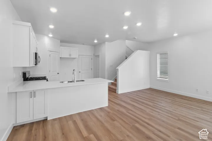 Open-concept living space with wood-finish flooring, white cabinetry, a kitchen island with an undermount sink, and recessed lighting