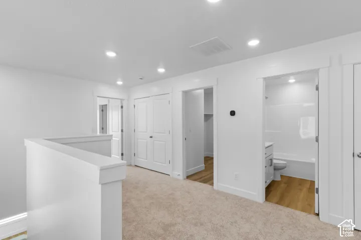 Loft area featuring neutral carpeting, white interior doors, bright recessed lighting, a built-in closet, and a full bathroom with a white vanity and tub/shower combination