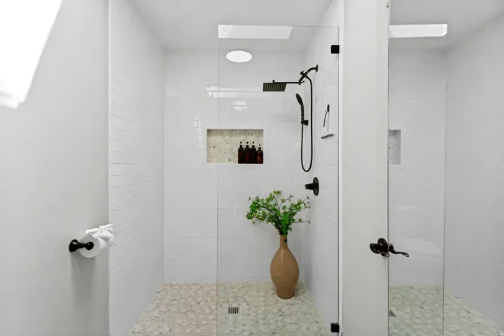 Walk-in shower featuring subway tile walls, pebble flooring, recessed shelving, and matte black fixtures