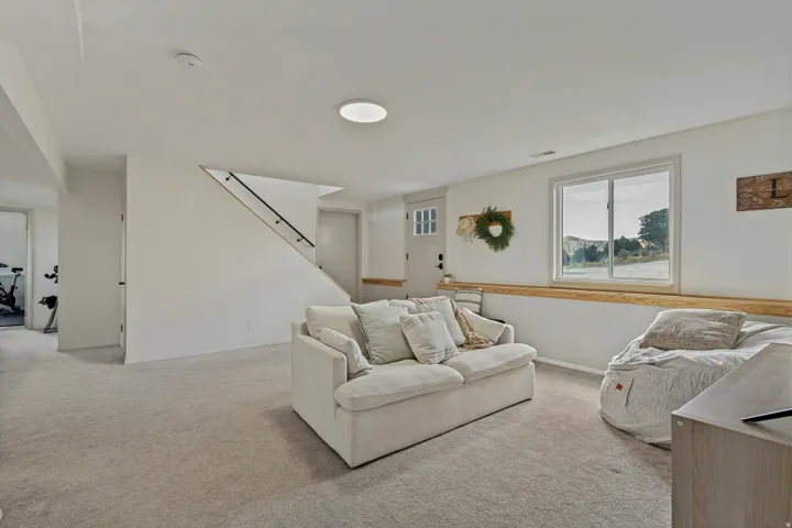 Expansive carpeted area featuring a window, built-in wooden shelf, interior door, and modern staircase with dark railing