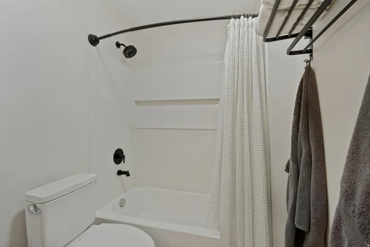 White bathtub with a matte black showerhead and faucet, accompanied by a white toilet and a wall-mounted towel rack