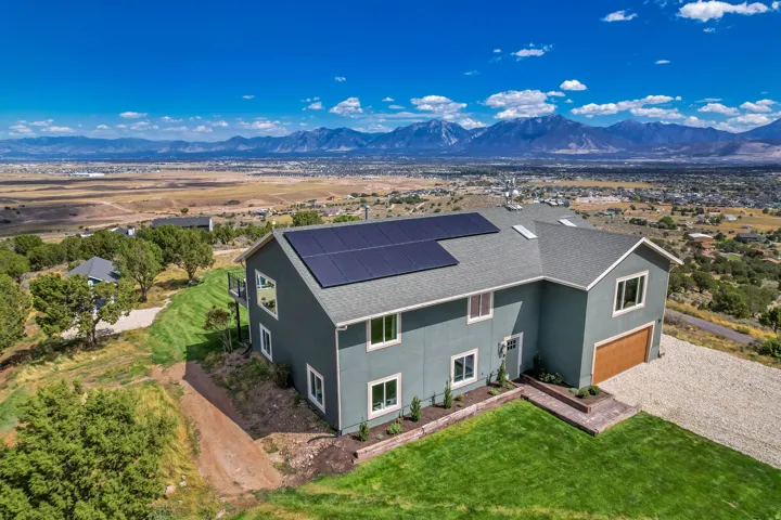 Two-story home with a wood-finish garage door, solar panel array, and a green lawn with landscaped beds