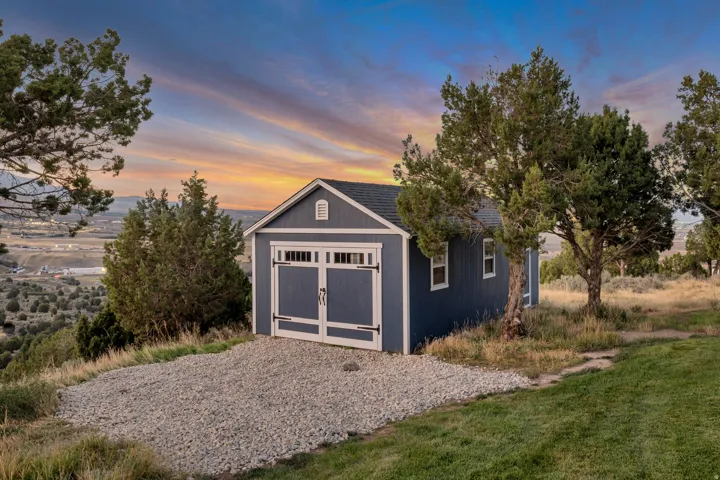 Detached storage shed with a gable roof, two windows, and double doors featuring decorative hardware