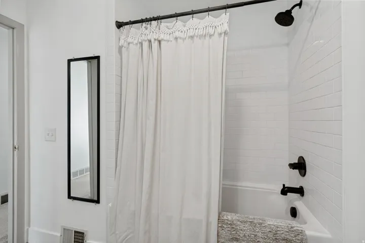Bathtub with subway tile surround, matte black shower fixtures, and a framed wall mirror