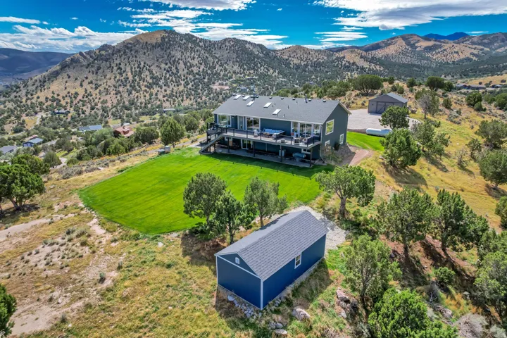 Expansive property featuring a multi-level dwelling, separate outbuilding, detached garage, manicured lawn, and mountainous backdrop