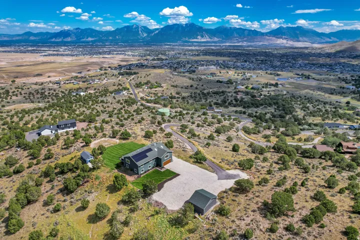 Expansive property featuring a residence with solar panels, a detached outbuilding, a gravel driveway, and a manicured lawn