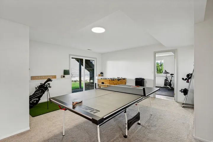 Carpeted recreation room with a circular ceiling light fixture, sliding glass door access to the exterior, and a separate room with a window