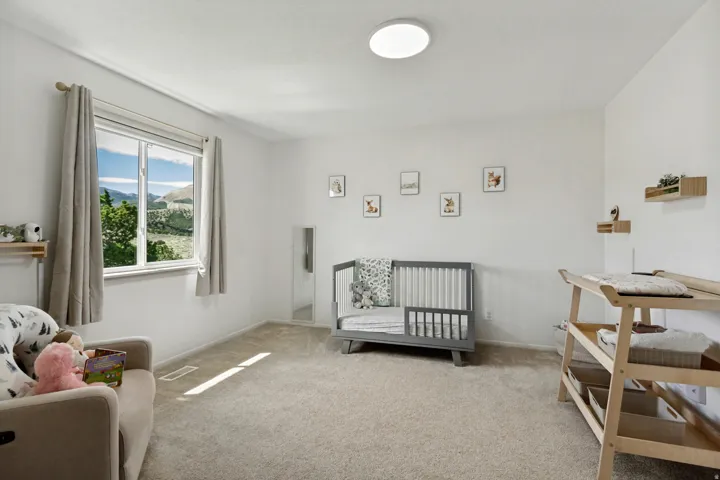Expansive room featuring neutral wall tones, broad window with natural scenery, light carpet flooring, and a flush-mount ceiling light