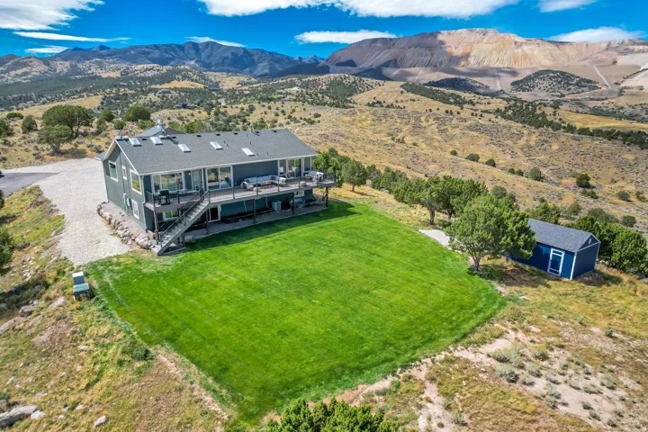 Expansive green lawn, multi-level deck, dark gray siding, multiple skylights, and a detached blue storage shed
