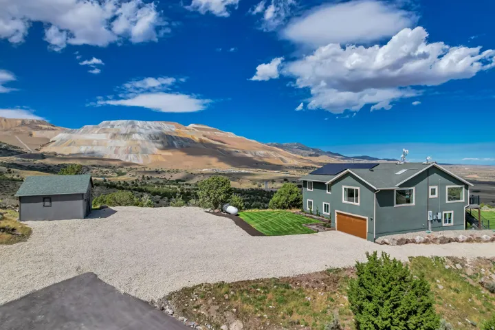 Two-story residence with a wood-finish garage door, solar panels, and an expansive gravel driveway