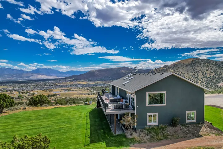 Expansive property with a large, elevated deck, dark gray siding, and a sloped terrain
