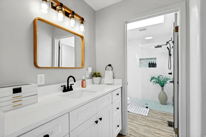 White vanity with integrated sink, matte black faucet, and gold-framed mirror with coordinating light fixture