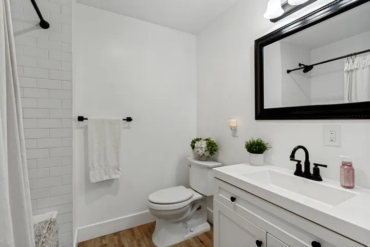 Bathroom featuring wood-finish flooring, white subway tile shower surround, a vanity with integrated sink, matte black fixtures, and a framed wall mirror