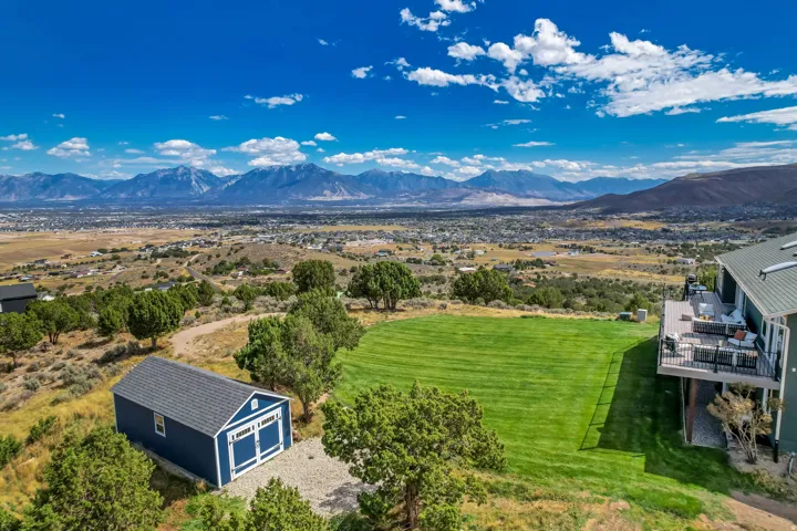 Expansive grassy yard, elevated outdoor deck, detached storage shed, surrounding natural landscape, and distant mountain range
