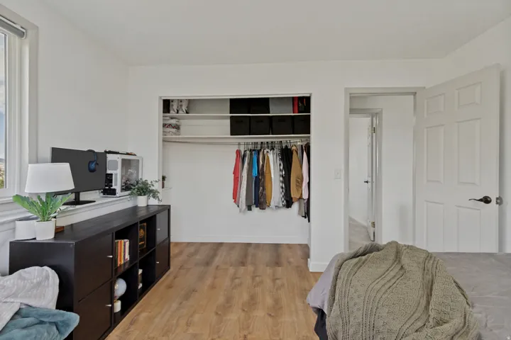 Wood-finish flooring, white paneled door with dark hardware, and an open closet with shelving and hanging rods