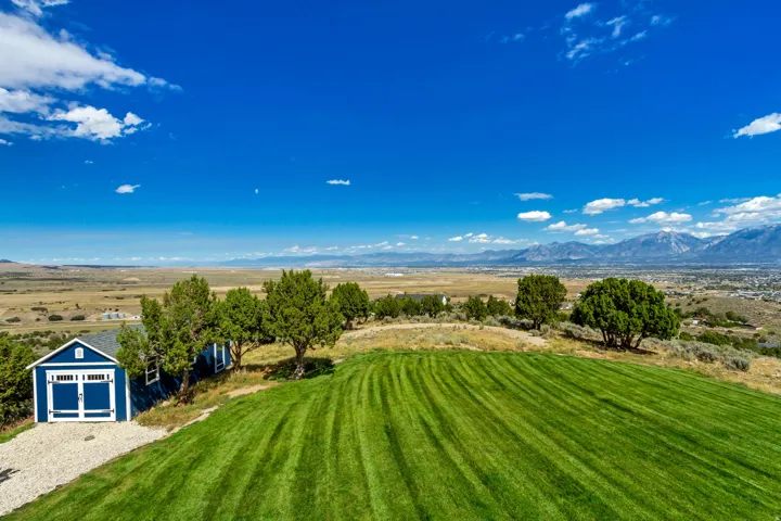 Expansive green lawn with mountain backdrop, accompanied by a detached blue shed with white trim and garage-style doors
