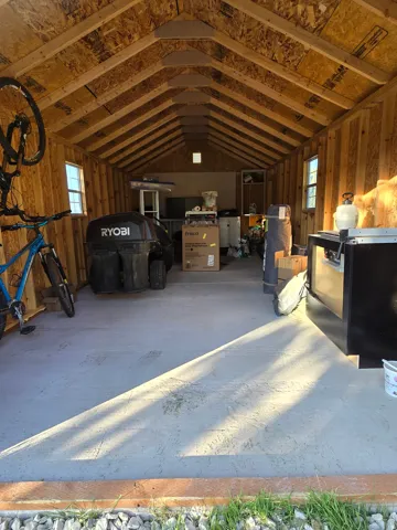 Spacious utility building featuring a vaulted ceiling with exposed rafters, multiple windows, and a concrete floor