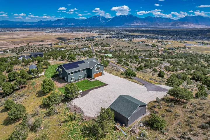 Two-story residence with solar panels, an attached garage, and a detached outbuilding, set on a landscaped lot with a gravel driveway