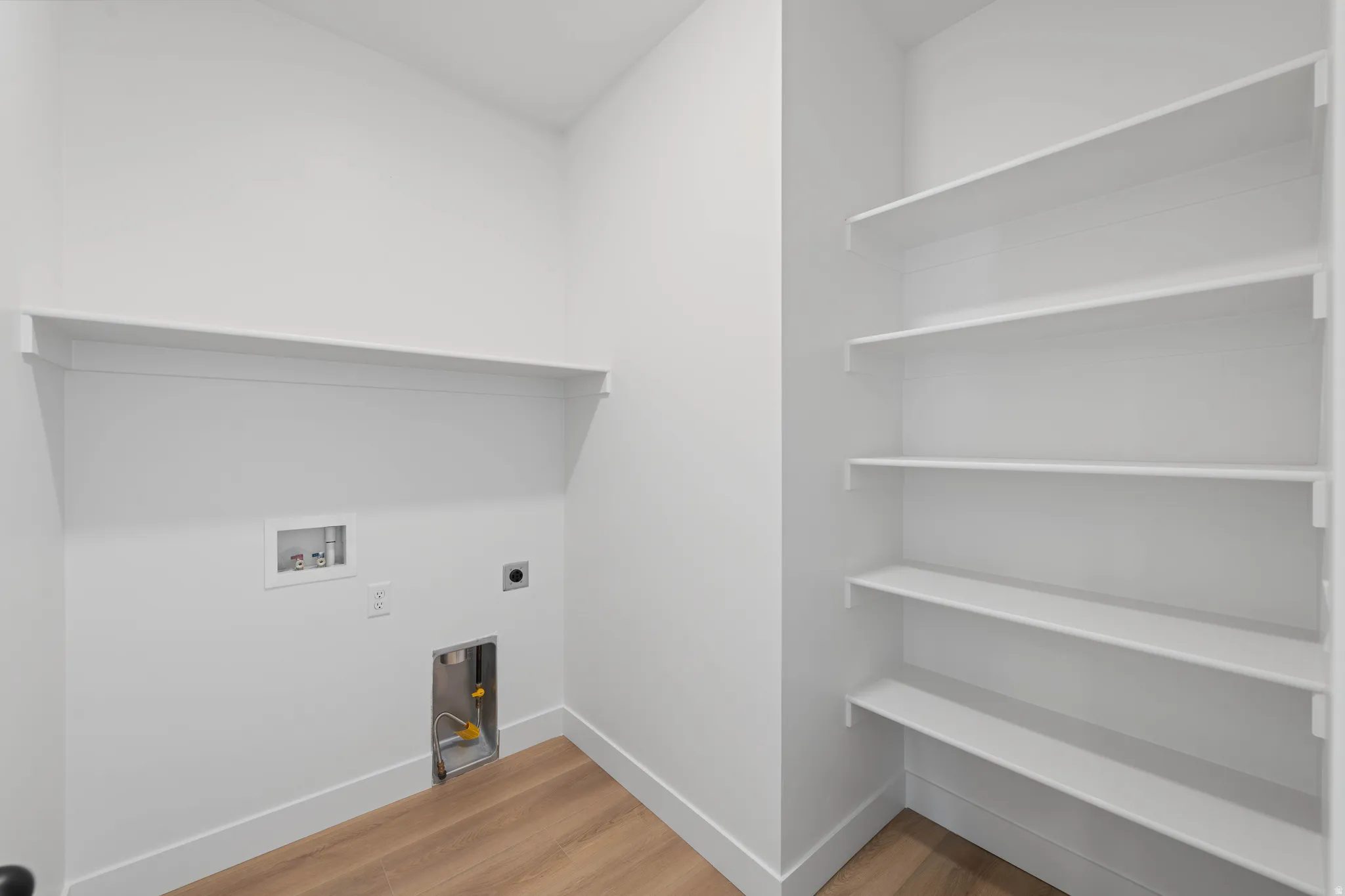 Dedicated utility area featuring wood-finish flooring, a built-in shelf, and white walls
