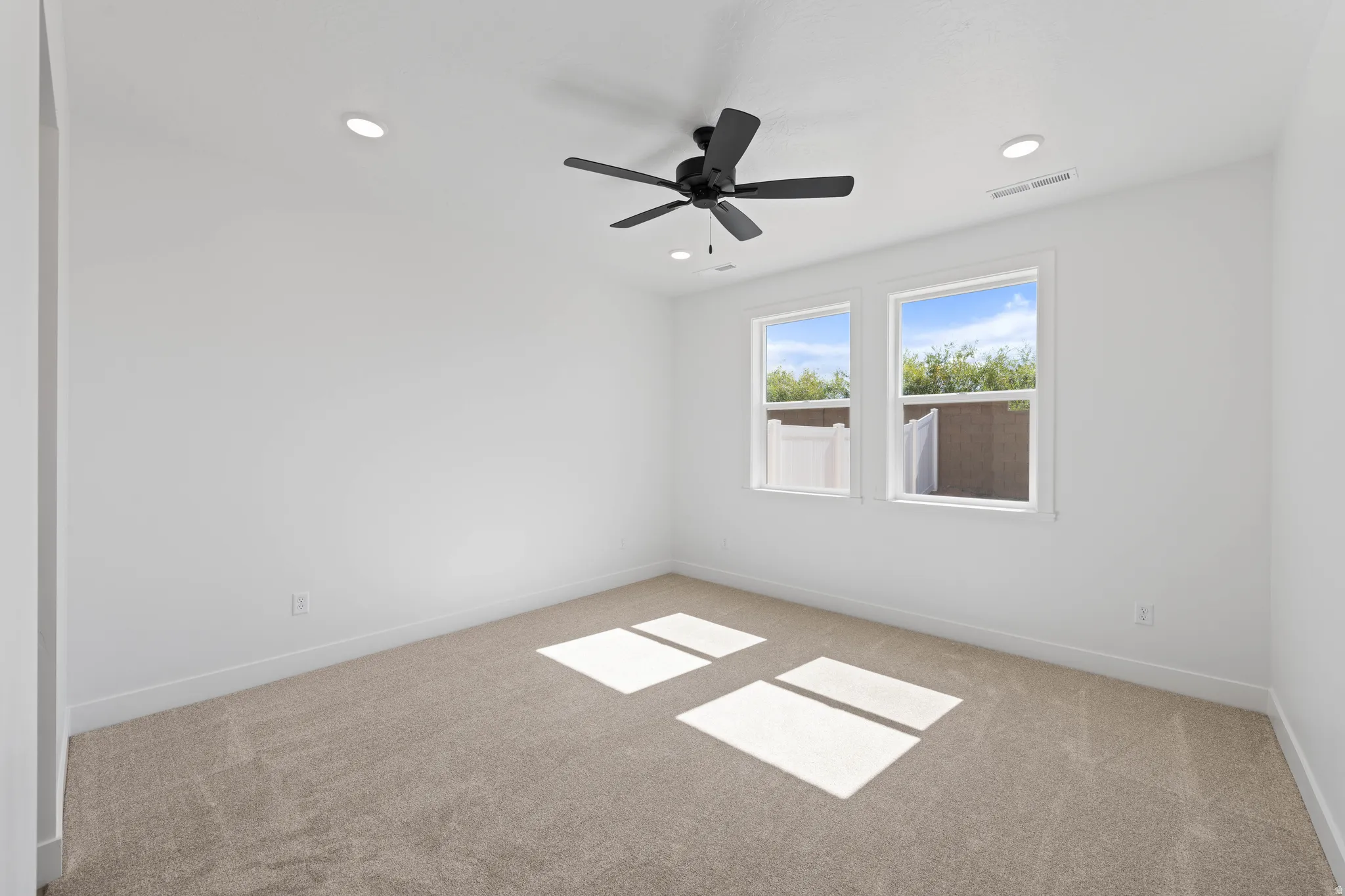 Recessed lighting, ceiling fan, white walls, two windows, and carpeting
