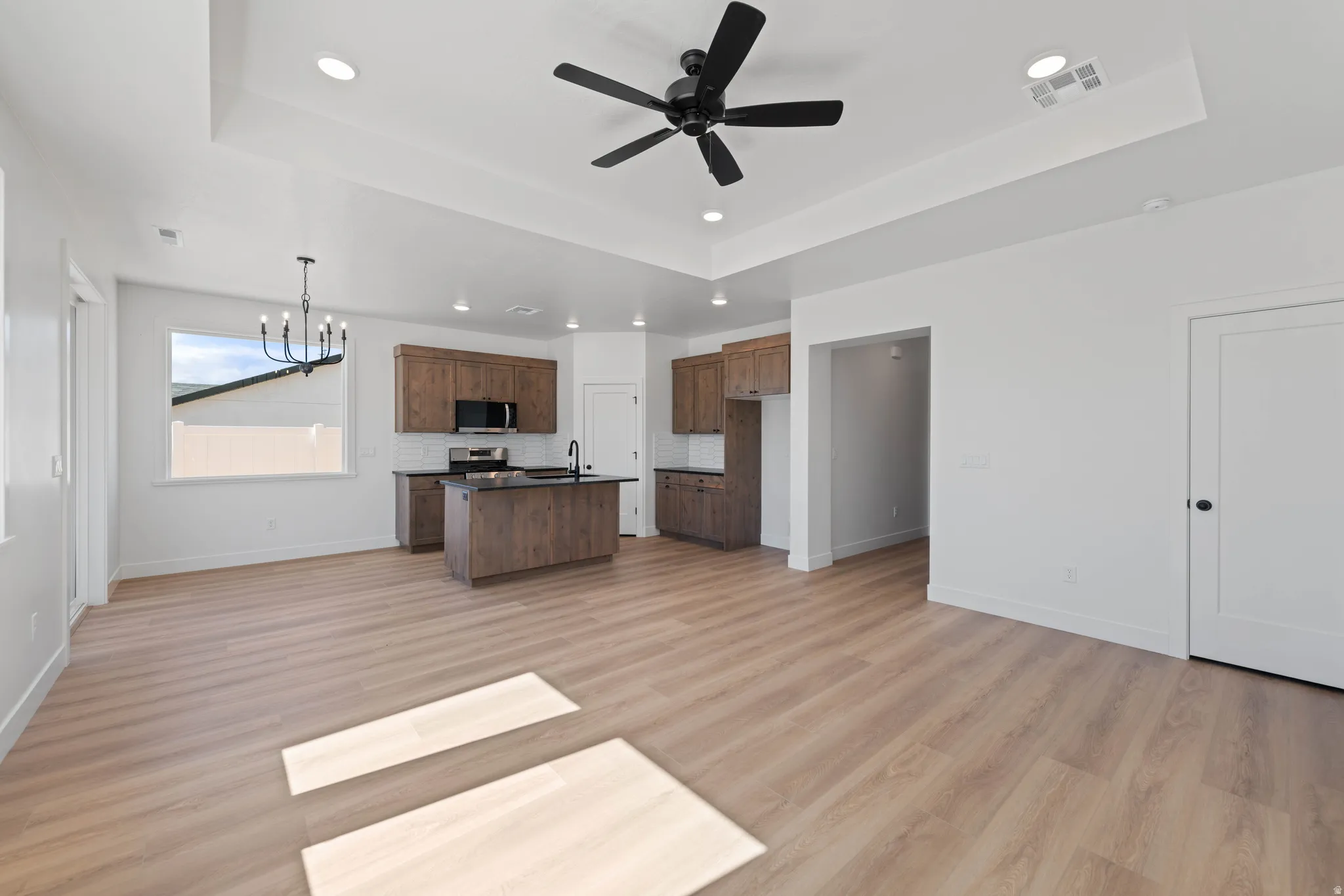 Kitchen and living area featuring a tray ceiling, wood-finish flooring, a kitchen island with a sink, wood cabinetry, and a black ceiling fan