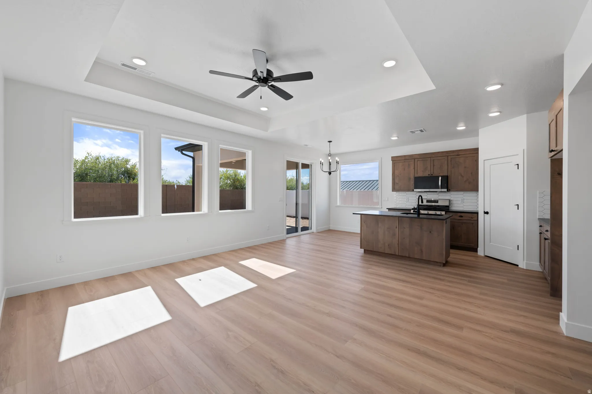 Tray ceiling with recessed lighting and ceiling fan, wood-finish flooring, three large windows, dark wood cabinetry, and a kitchen island with dark countertops