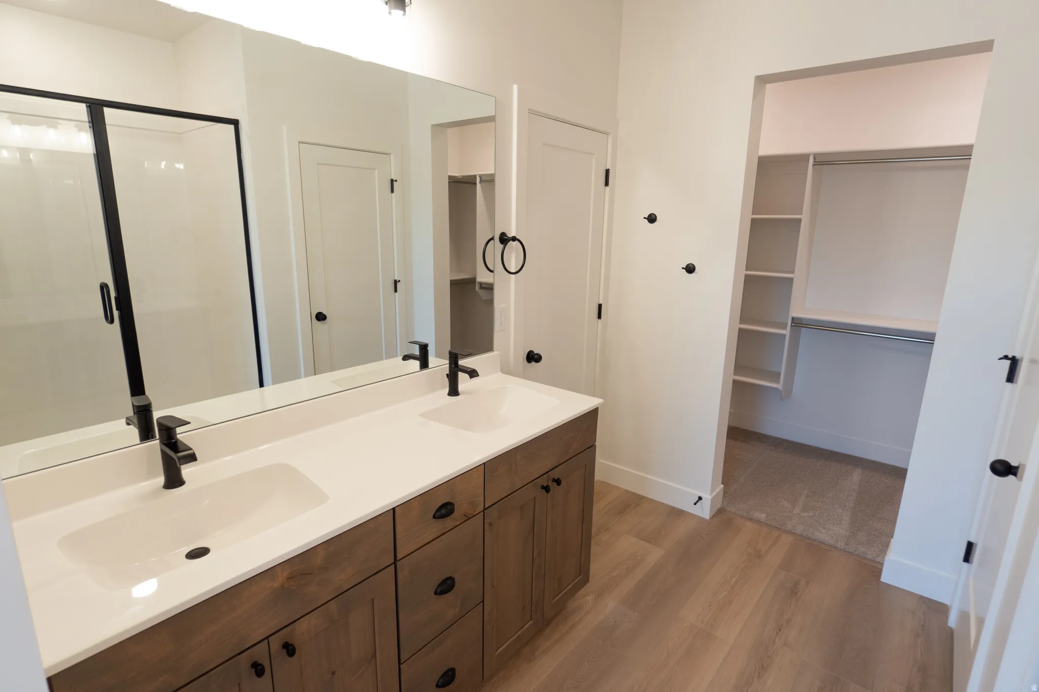 Dual vanity with wood-finish cabinetry, white countertops, and matte black fixtures