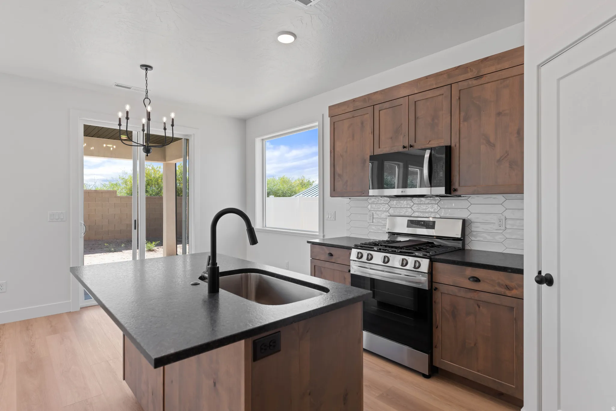 Kitchen featuring an island with a stainless steel sink and matte black faucet, wood-finish cabinetry, stainless steel appliances, and a tiled backsplash