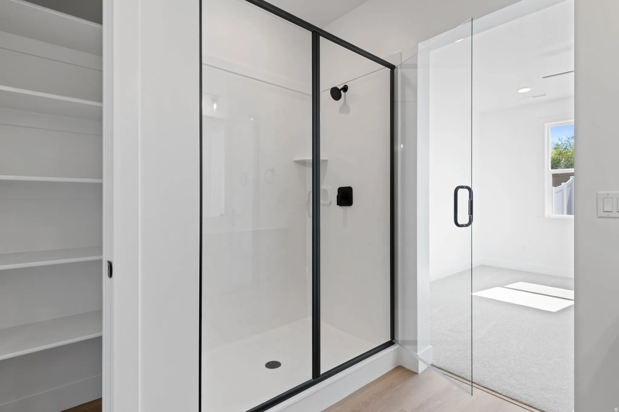 Walk-in shower with black-framed glass enclosure, matte black shower fixtures, and ample built-in shelving
